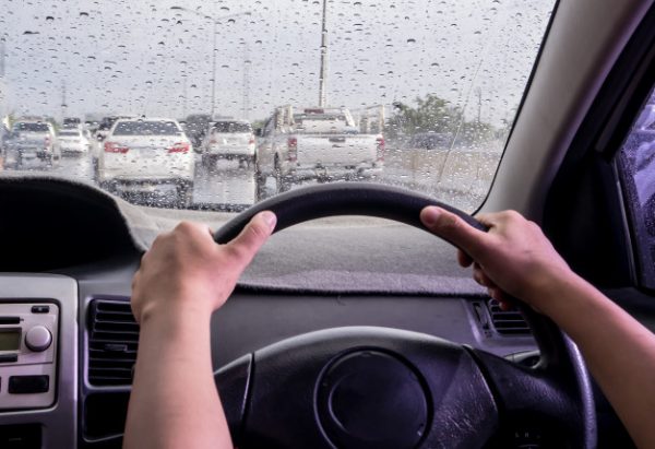 Driver's view through a rainy windshield with hands on the steering wheel.