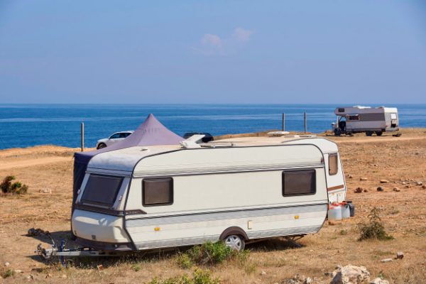 Vintage caravan parked on a grassy cliff overlooking the ocean.