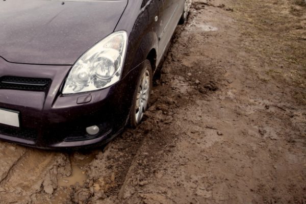 Close-up of a red car stuck in mud or deep tire ruts.