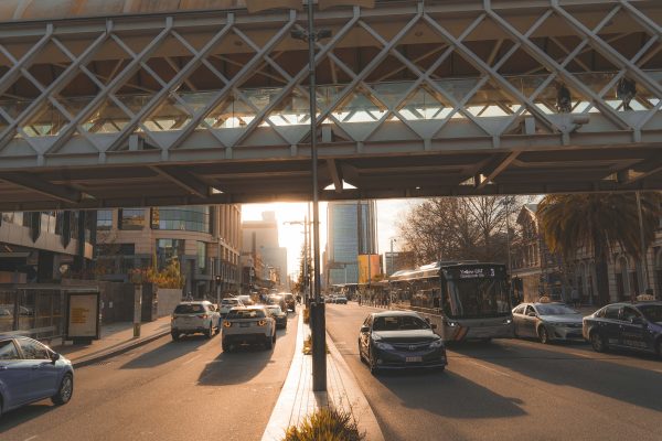 Traffic on a sunny urban road driving under a highway overpass.