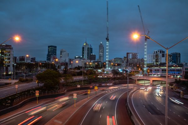 City skyline at dusk with light trails from cars on a wet highway.
